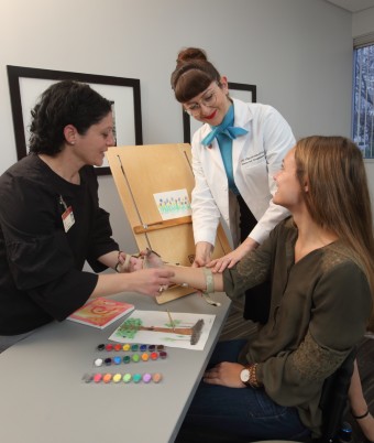 Dr. Samia Rafeedie and OTD student Antonietta Iannaccone demonstrate to Master's student Rachael Paszotta how to use a wrist-driven wrist-hand orthosis when working with a client who has a spinal cord injury and loves to paint.Photo credit: Phil Channing